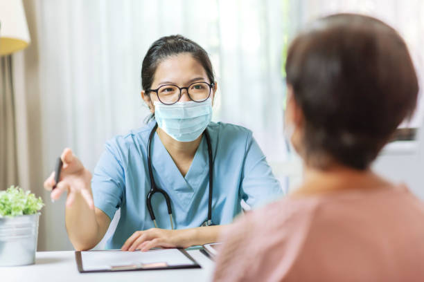 aziatische arts die van de vrouw aan vrouwelijke patiënt bij het ziekenhuis spreekt - arts vrouw mondkapje stockfoto's en -beelden