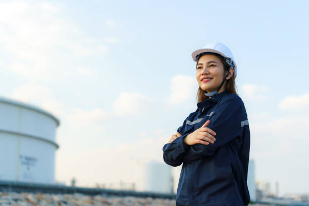 Asian woman engineer arm crossed and smile with confident looking forward to future with oil refinery plant factory in background. stock photo