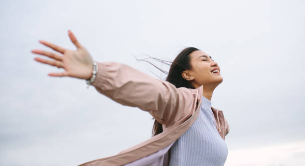 Asian woman enjoying nature standing with open arms Portrait of a smiling woman standing outdoors with stretched arms on a cold winter morning. Side view close up of a happy woman standing outdoors with open arms and closed eyes. philippines girl stock pictures, royalty-free photos & images