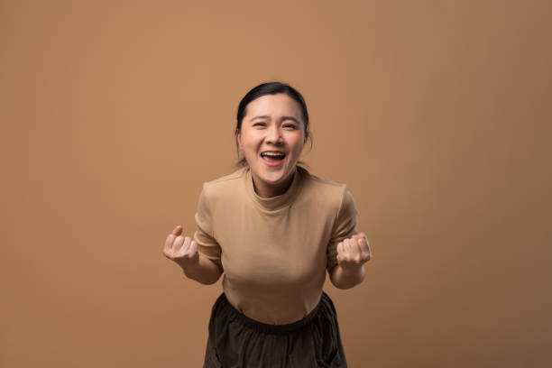 Asian woman happy make a winning gesture isolated on beige background. stock photo
