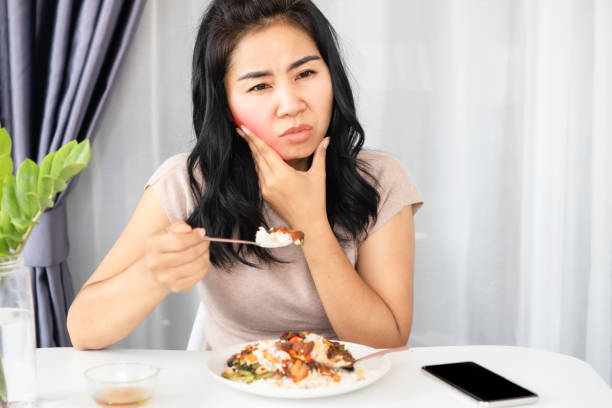 Asian woman having a problem with toothache, sensitive tooth while eating food stock photo
