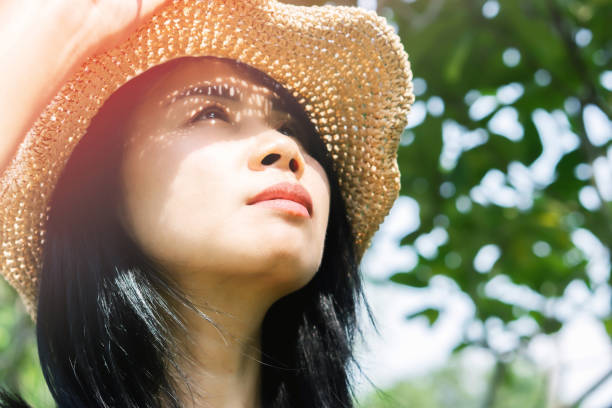 Asian woman in summer standing outdoors on sunny day with UV sunlight burning on stock photo