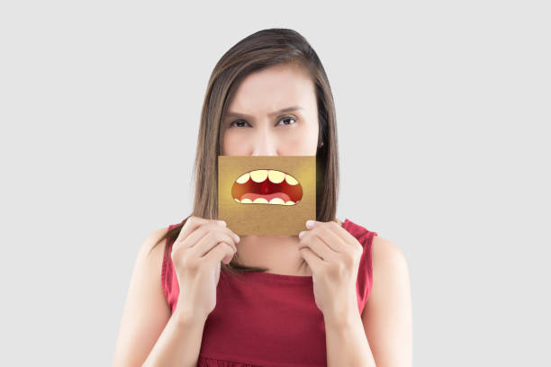 Asian woman in the red shirt holding a brown paper with the yellow teeth cartoon picture of his mouth against the gray background, Bad breath or Halitosis, The concept with healthcare gums and teeth stock photo