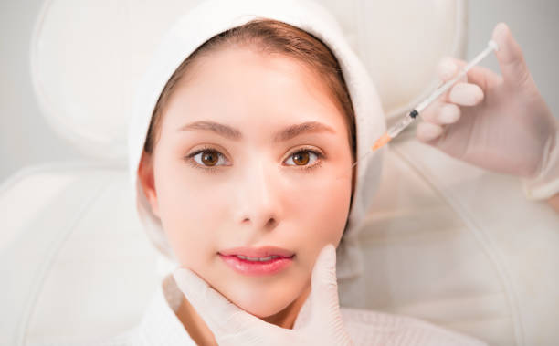 Asian woman lying on bed and cosmetologist does injections to face augmentation for anti wrinkle in beauty clinic. stock photo