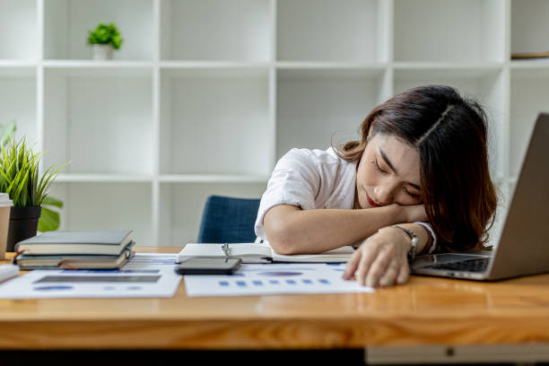 Asian woman napping at her desk, Businesswoman snoozing at her desk after working for a long time causing fatigue and sleepiness, she is resting. Hard work concept. stock photo