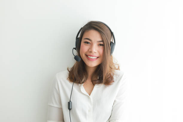 Asian woman on white shirt speak with headphone and using laptop on white background smile and happy face operator concept stock photo