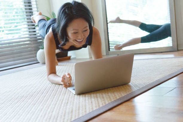 Asian woman practicing yoga at home Asian woman practicing yoga at home, she is following an online video class personal trainer online stock pictures, royalty-free photos & images