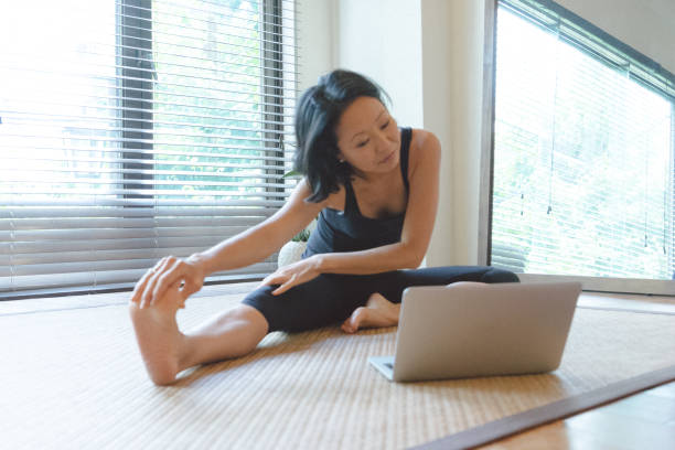 Asian woman practicing yoga at home Asian woman practicing yoga at home, she is following an online video class asian yoga pants stock pictures, royalty-free photos & images