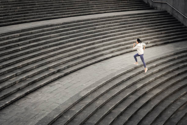 Asian woman running up outdoor stairway in city stock photo