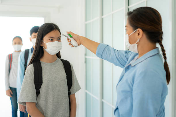 asian woman teacher using thermometer temperature screening student for fever against the spread of covid-19 while student coming back to school, new normal and education concept. - teacher back to school imagens e fotografias de stock