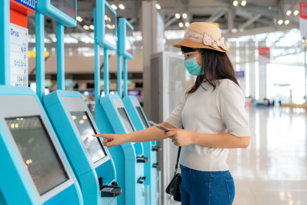Asian woman traveler wearing mask using self check-in kiosk in airport terminal during coronavirus (COVID-19) pandemic prevention when travel abroad. New normal travel  concept Asian woman traveler wearing mask using self check-in kiosk in airport terminal during coronavirus (COVID-19) pandemic prevention when travel abroad. New normal travel  concept self service photos stock pictures, royalty-free photos & images