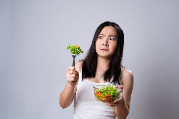 Asian woman trying to eat salad for diet isolated over white background. stock photo