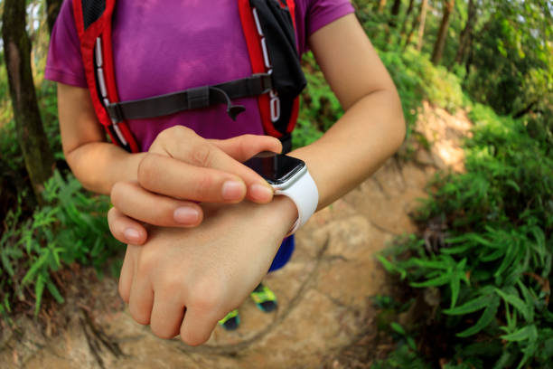 Asian woman ultramarathon runner set the smartwatch before running at tropical rainforest trail stock photo