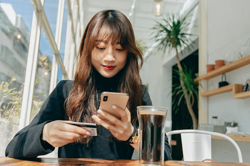 Asian woman using smartphone and credit card for online shopping at cafe