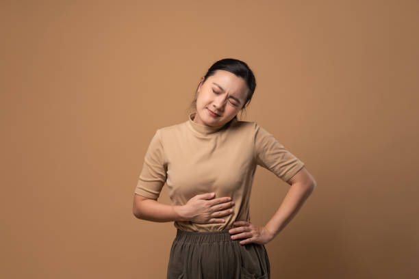 Asian woman was sick with stomach ache standing isolated on beige background. stock photo