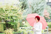 事務所ビルの庭に赤い傘とアジアの女性が歩いています。