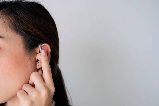 asyalı kadınlar daha iyi duyabilmek için işitme cihazı takıyor, parmağınızla işitme cihazına dokunuyor - hearing aids stok fotoğraflar ve resimler