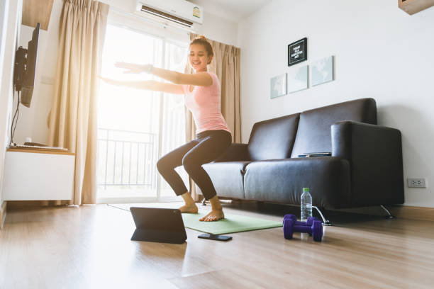 Asian women workout at home and watch videos for fitness instruction. A beautiful woman exercising at home with Squat in the living room of the house. stock photo