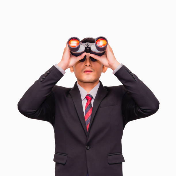 Asian young businessman standing and looking through binoculars stock photo