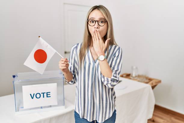Asian young woman at political campaign election holding japan flag covering mouth with hand, shocked and afraid for mistake. surprised expression Asian young woman at political campaign election holding japan flag covering mouth with hand, shocked and afraid for mistake. surprised expression how do you say shut up in japanese stock pictures, royalty-free photos & images