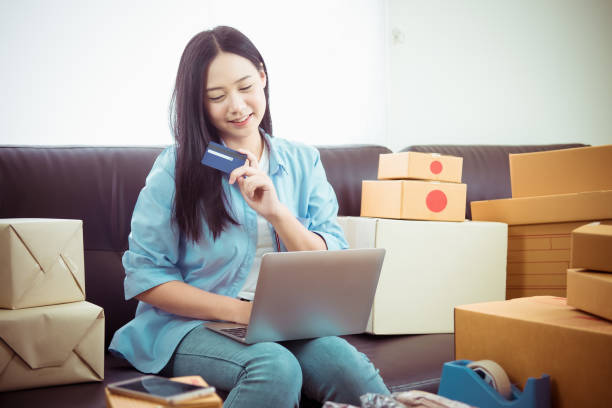Asian young woman business work at home holding credit card and using laptop smart phone for online shopping and sale.small and medium enterprise business ,sale online concept,happy to sale stock photo