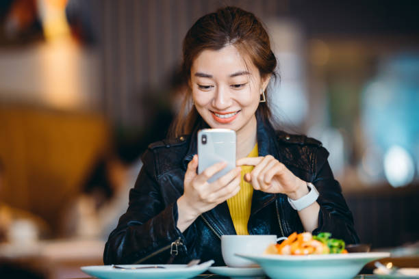 レストランで携帯電話を使用してアジアの若い女性。 - iphone ストックフォトと画像