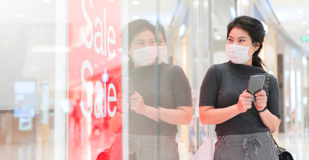 Asian young woman looking through a plexiglass store with a sale promotion