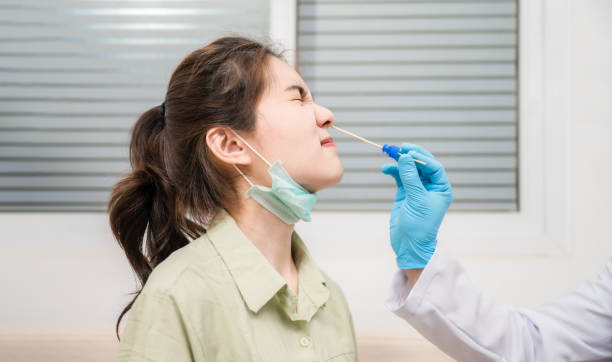 Asian young woman wear mask sitting on couch and checked in nasal cavity coronavirus from doctor by swab method in hospital. stock photo