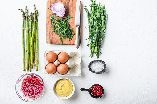 Asparagus eggs and french dressing ingredients with dijon mustard, onion chopped in red vinegar  taragon on white textured background, top view