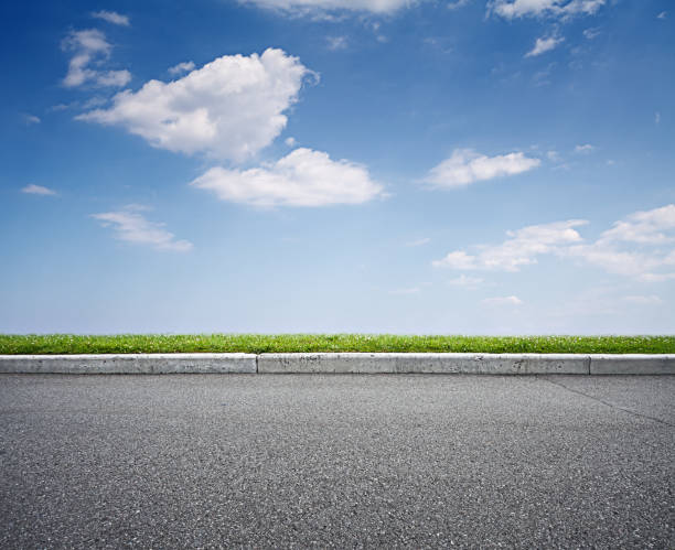 asphalt road and blue sky above green grass stock photo