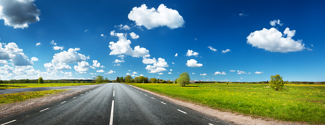 Asphalt road on the dandelion field with beautiful clouds in the sky