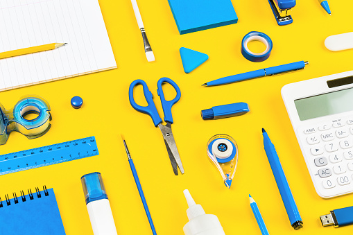 Assorted office and school white and blue stationery on bright yellow background. Organized knolling for back to school or education and craft concept. Selective focus