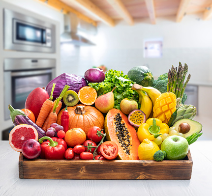 Assorted vegetables and fruits in wooden crate box in a kitchen indoor background