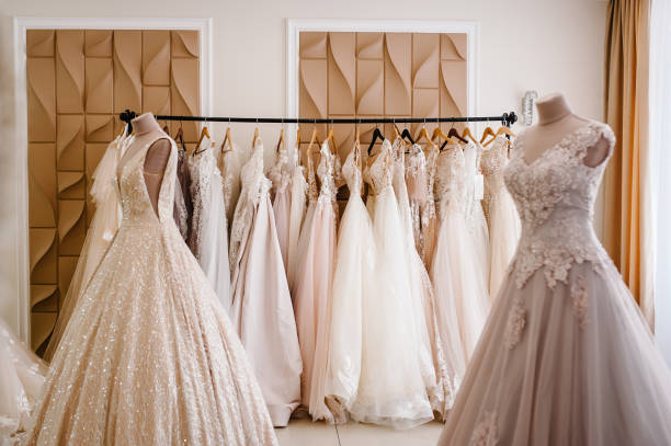 Assortment of dresses hanging on a hanger on the background studio. Fashion wedding trends. Interior of wedding shop. Assortment of dresses hanging on a hanger on the background studio. Fashion wedding trends. Interior of wedding shop. wedding store stock pictures, royalty-free photos & images