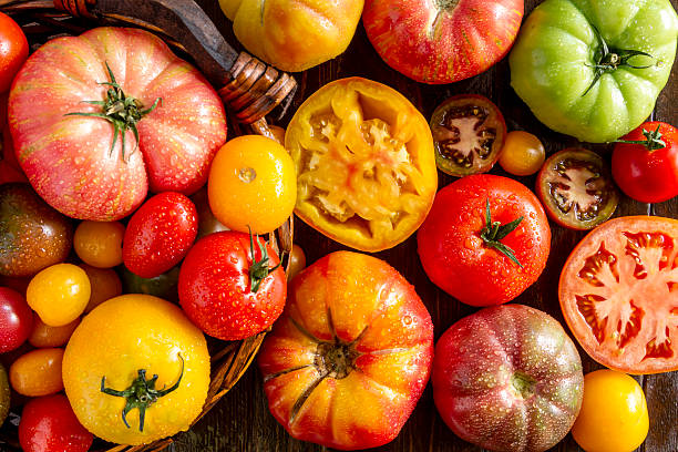 Assortment of Fresh Heirloom Tomatoes Colorful assortment of fresh organic whole and cut heirloom tomatoes sitting on wooden table ripe stock pictures, royalty-free photos & images