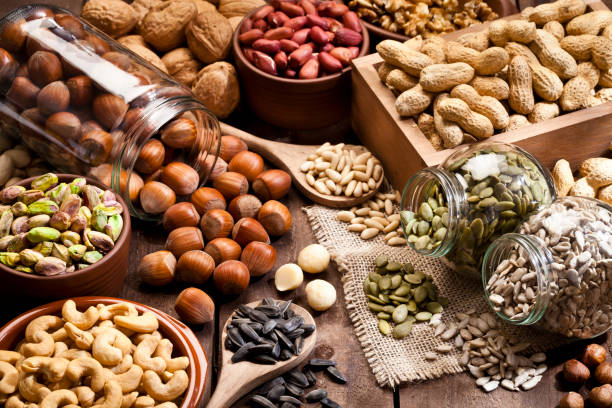 Assortment of nuts on rustic wood table. Horizontal shot of a rustic wood table filled with a large assortment of nuts like pistachios, hazelnut, pine nut, almonds, pumpkin seeds, sunflower seeds, peanuts, cashew and walnuts. Some nuts are in brown bowls and others in glass jars. Predominant color is brown. DSRL studio photo taken with Canon EOS 5D Mk II and Canon EF 100mm f/2.8L Macro IS USM nut food stock pictures, royalty-free photos & images