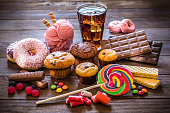 Assortment of products with high sugar level like candies, gummy candies, donuts, soda, chocolate, lollipop, wafers and cupcakes on rustic wooden table. Low key DSLR photo taken with Canon EOS 6D Mark II and Canon EF 24-105 mm f/4L