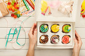 Set of colorful cupcakes in delivery box in female hands on white background. Sweet snacks for holiday celebration and colorful decorations for birthday party, top view