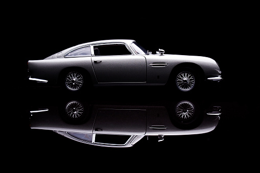 Beaconsfield, UK - November 2, 2015: A model of Aston Martin's iconic DB5 sits on a reflective base against a black background. Released in 1963, the car found global fame as the gadget-laden transport of the world's most famous secret agent, James Bond.