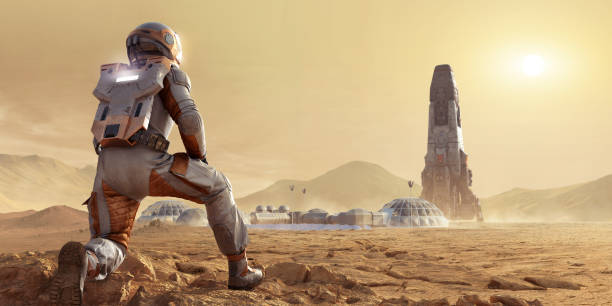 Astronaut On Mars Kneeling and Looking At Base Camp Settlement and Rocket In Mars Rocky Environment stock photo