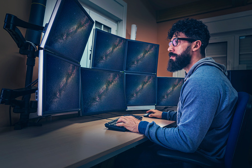 Astronomer in control panel room multi screen sitting profile with beard