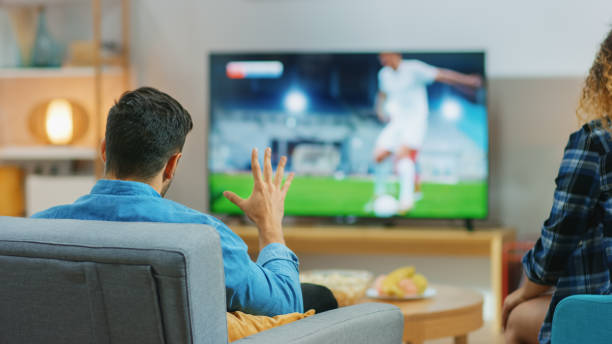 在家裡年輕夫婦在電視上觀看緊張的足球比賽時刻，他們擔心，傢伙試圖耐心和積極顯示棕櫚。後視圖拍攝。 - soccer news 個照片及圖片檔