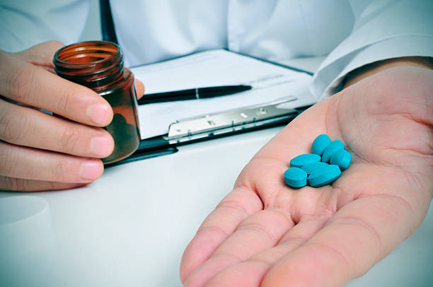 at the doctors office a doctor sitting in a desk with a pile of blue pills in his hand anti impotence tablet stock pictures, royalty-free photos & images