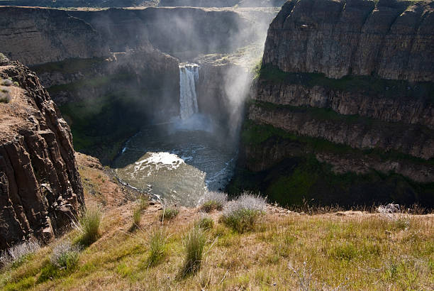 Morning Mist Over Palouse Falls At the end of the last ice age, the great Missoula Flood swept across eastern Washington leaving the unique scablands we see today. Palouse Falls, 198 feet high, remains as one of the magnificent remnants of the flood. As of February 12, 2014, Palouse Falls was named as Washington State's official waterfall. The powerful waterfall is on the Palouse River, a few miles upstream from its confluence with the Snake River. This view off morning mist over the falls was captured from Palouse Falls State Park, Washington State, USA. jeff goulden rainbow stock pictures, royalty-free photos & images