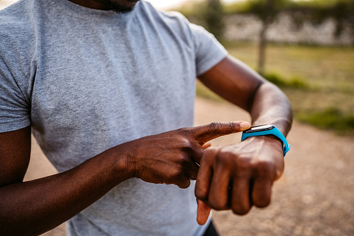Athlete check fitness tracker on smartwatch or playing his music playlist after training in nature.