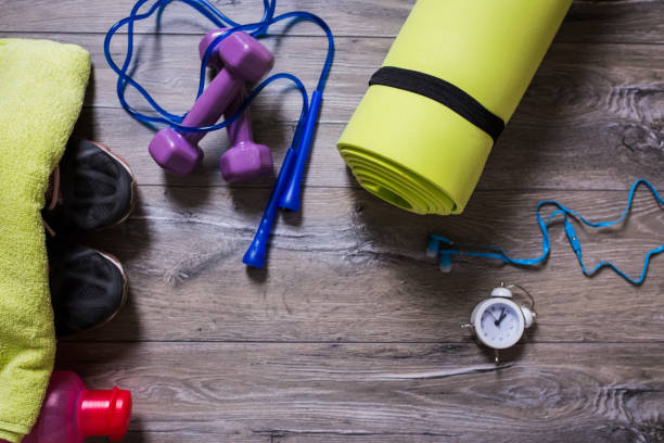 athlete's set with pink dumbbells, bottle of water, jump rope on blue yoga mat and yellow sneakers on pastel blue background - mitrovic stockfoto's en -beelden