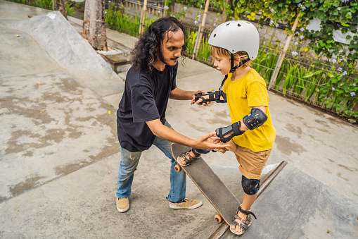 Athletic boy learns to skateboard with a trainer in a skate park. Children education, sports.