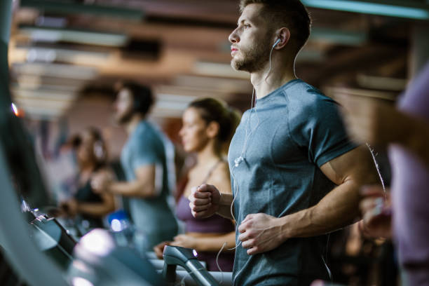 atletyczny człowiek słuchający muzyki podczas biegania na bieżni w siłowni. - gym zdjęcia i obrazy z banku zdjęć