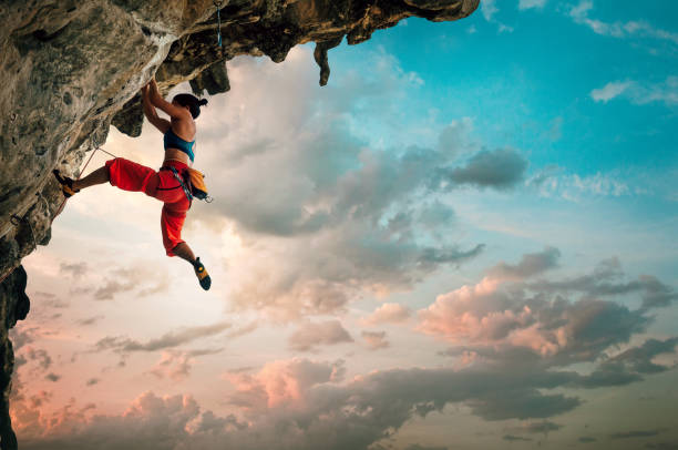Athletic Woman climbing on overhanging cliff rock with sunrise sky background stock photo