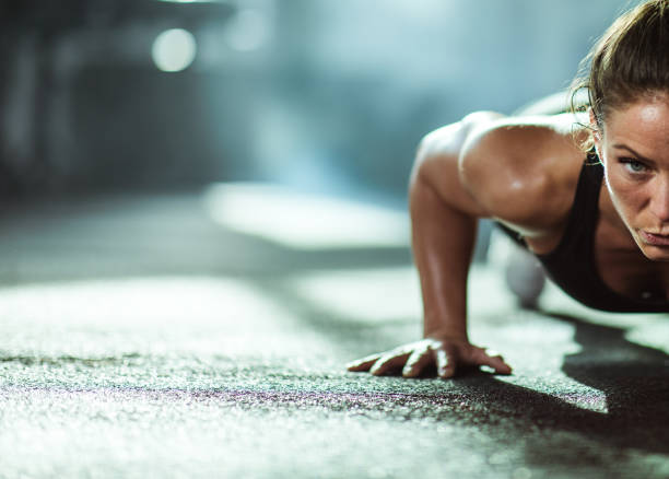 Athletic woman exercising push-ups in a health club. Young female athlete exercising push-ups with in a gym. Copy space. athleticism stock pictures, royalty-free photos & images